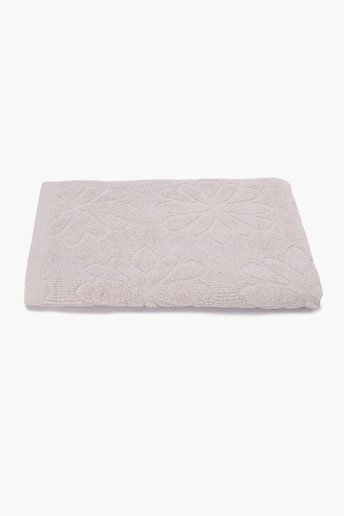 Folded beige cotton towel with floral textured pattern on a white background