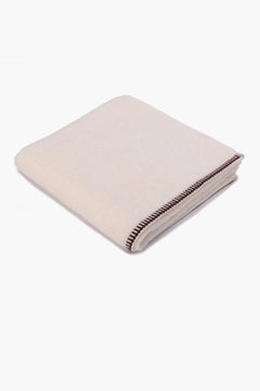 Folded beige cotton towel with brown stitched border on white background