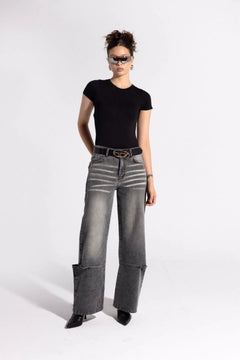 Woman in a black fitted t-shirt and wide-leg faded gray jeans with sunglasses in studio
