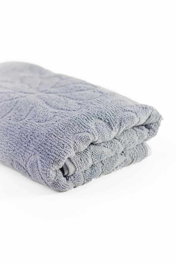 Folded light grey cotton towel with textured floral pattern on a white background