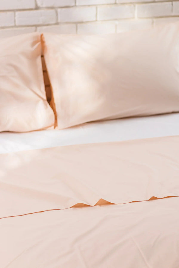Soft peach cotton bed sheets and pillowcases on a bed with a white brick wall background