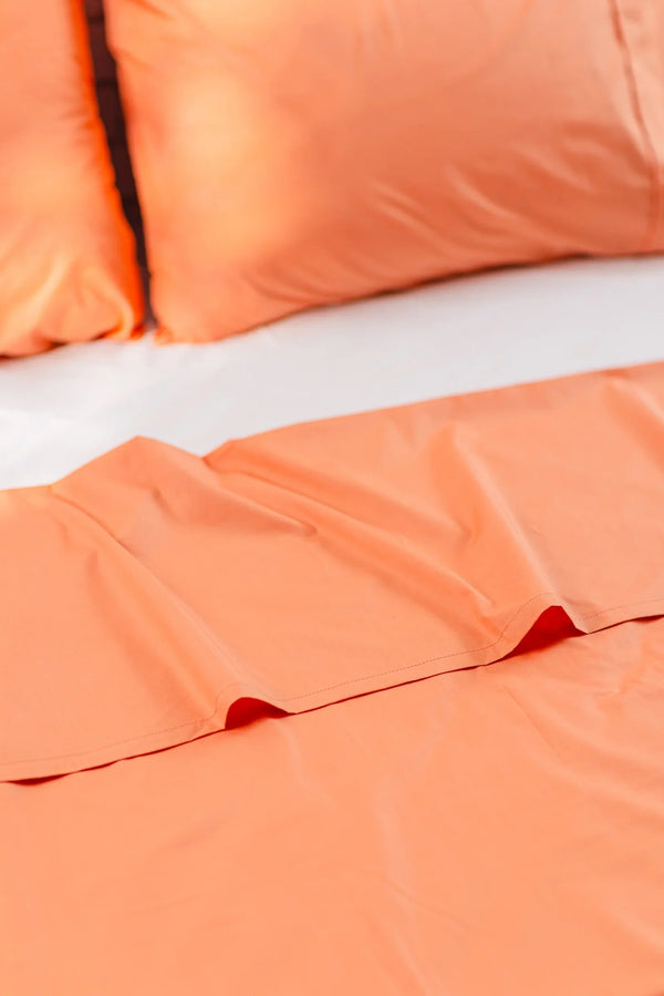 Peach orange cotton bed sheet set with matching pillowcases on a bed