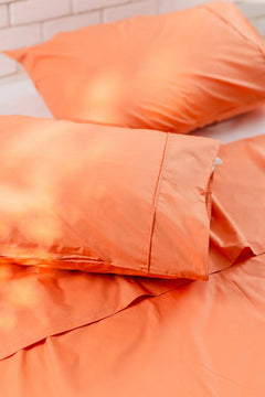 Soft orange cotton pillowcases and bed sheets on a bed, close-up.