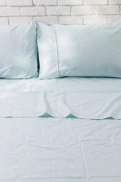 Light blue cotton bed sheet set with two pillows on bed against white brick wall