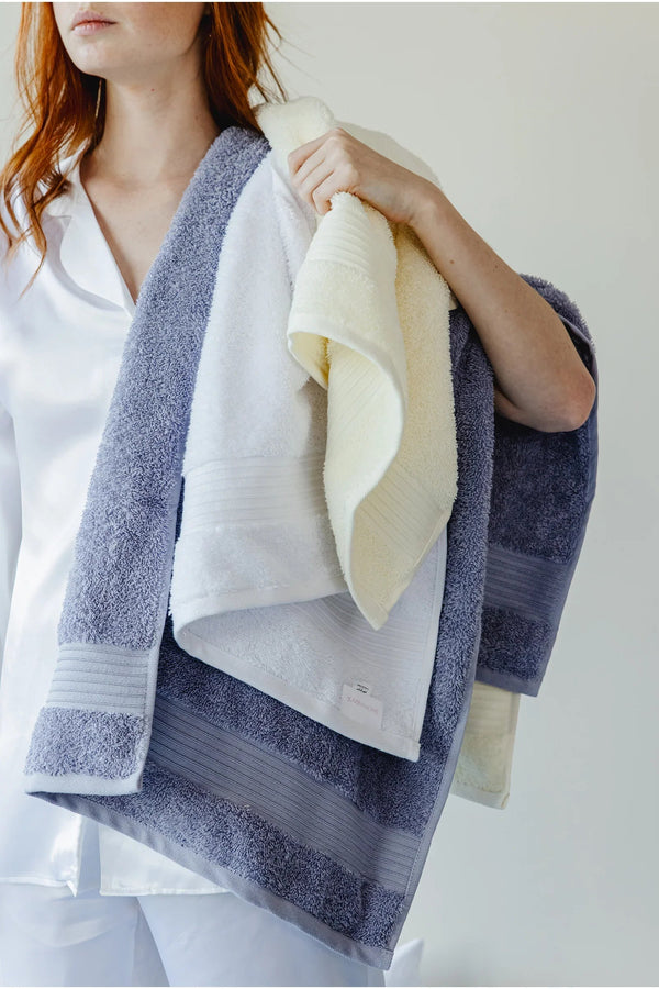 Woman in white pajamas holding soft cotton bath towels in pastel colors