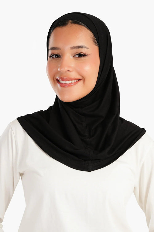 Woman wearing a black cotton hijab and white top, smiling against a plain background