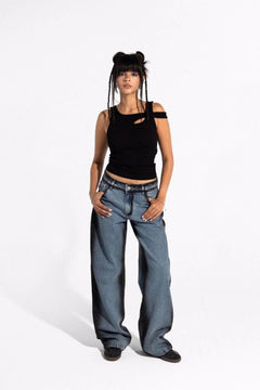Woman in wide-leg blue jeans and black sleeveless top posing against a white background