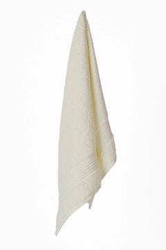cream-colored cotton towel with textured border hanging on white background