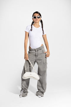 Woman in white bodysuit, gray double zipper jeans, sunglasses, holding white handbag
