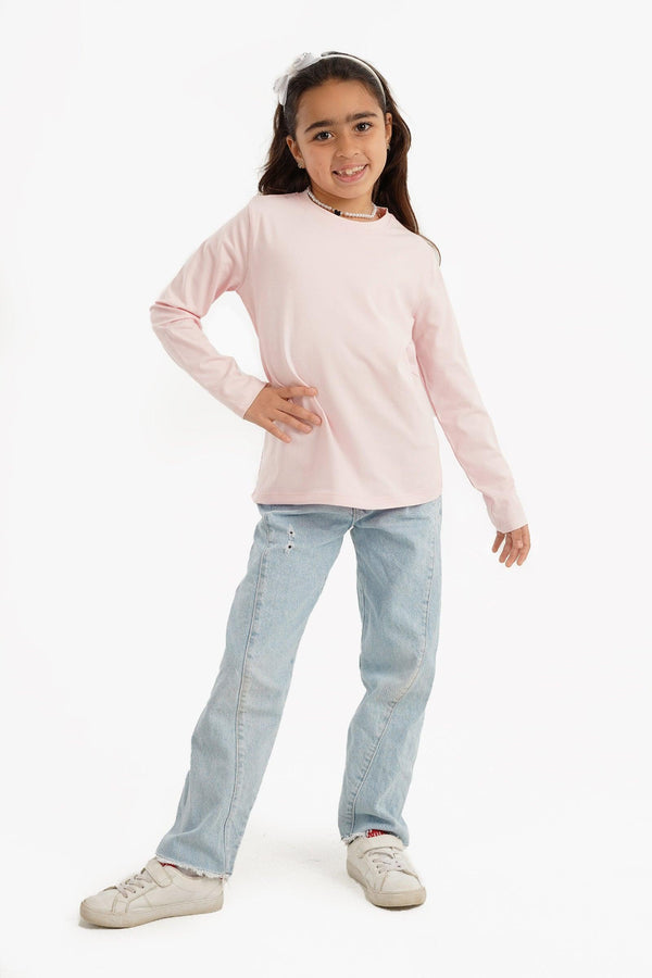 Girl wearing light pink long sleeve top, light blue jeans, and white sneakers, standing and smiling