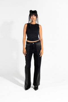 Woman wearing black patchwork jeans and a sleeveless black top, standing in studio
