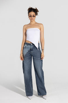 Woman in wide-leg unzipped jeans and white asymmetrical top, posing in a studio.