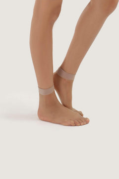 Sheer nude short voile socks on woman's feet against a white background