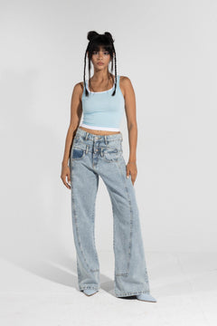 Woman in light blue tank top and high-waisted wide leg jeans posing on white background